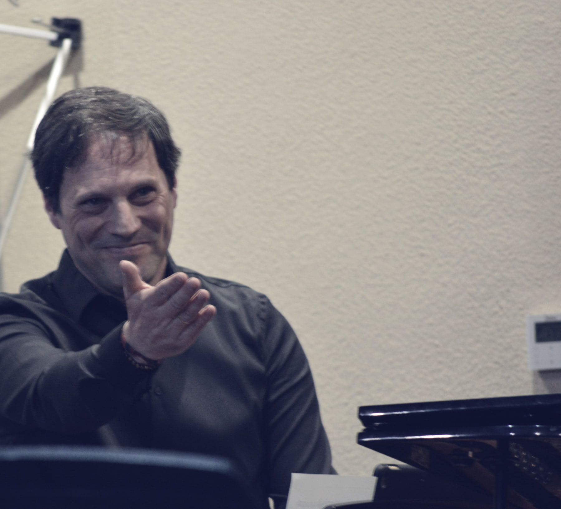 Sergio Cano Ortiz en el aula junto al piano, sonriendo y señalando con la mano.