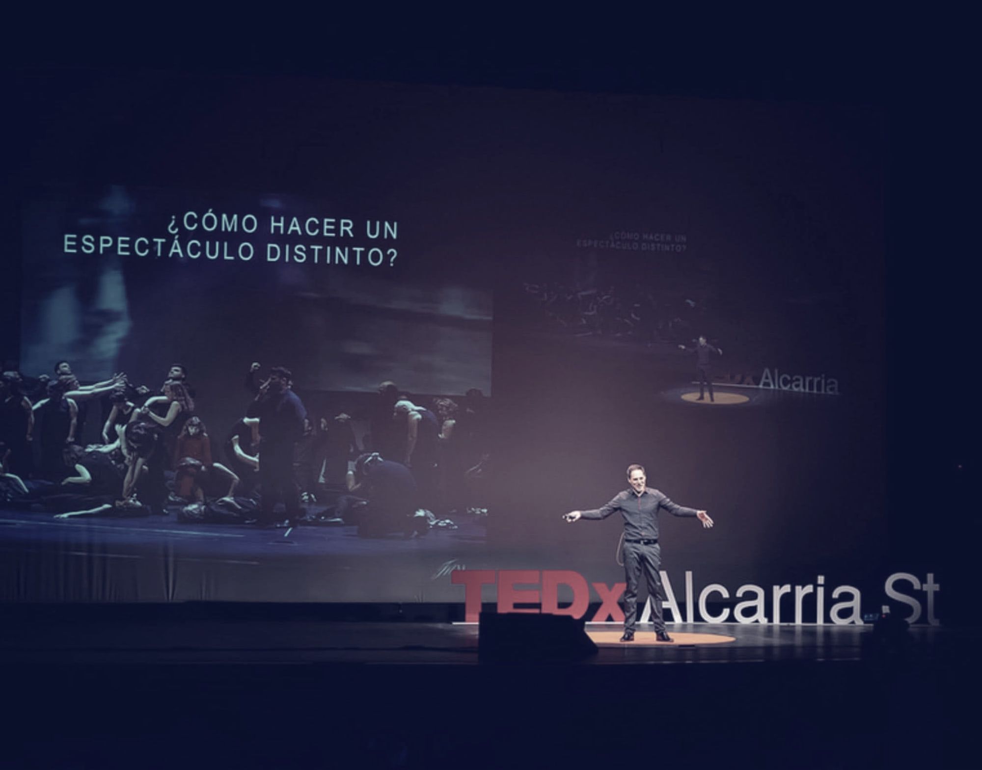 Sergio Cano Ortiz con los brazos abiertos en el escenario de TEDxAlcarriaSt; en la pantalla, la pregunta «¿Cómo hacer un espectáculo distinto?».